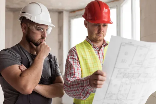 Deux ouvriers casqués consultant un plan sur un chantier